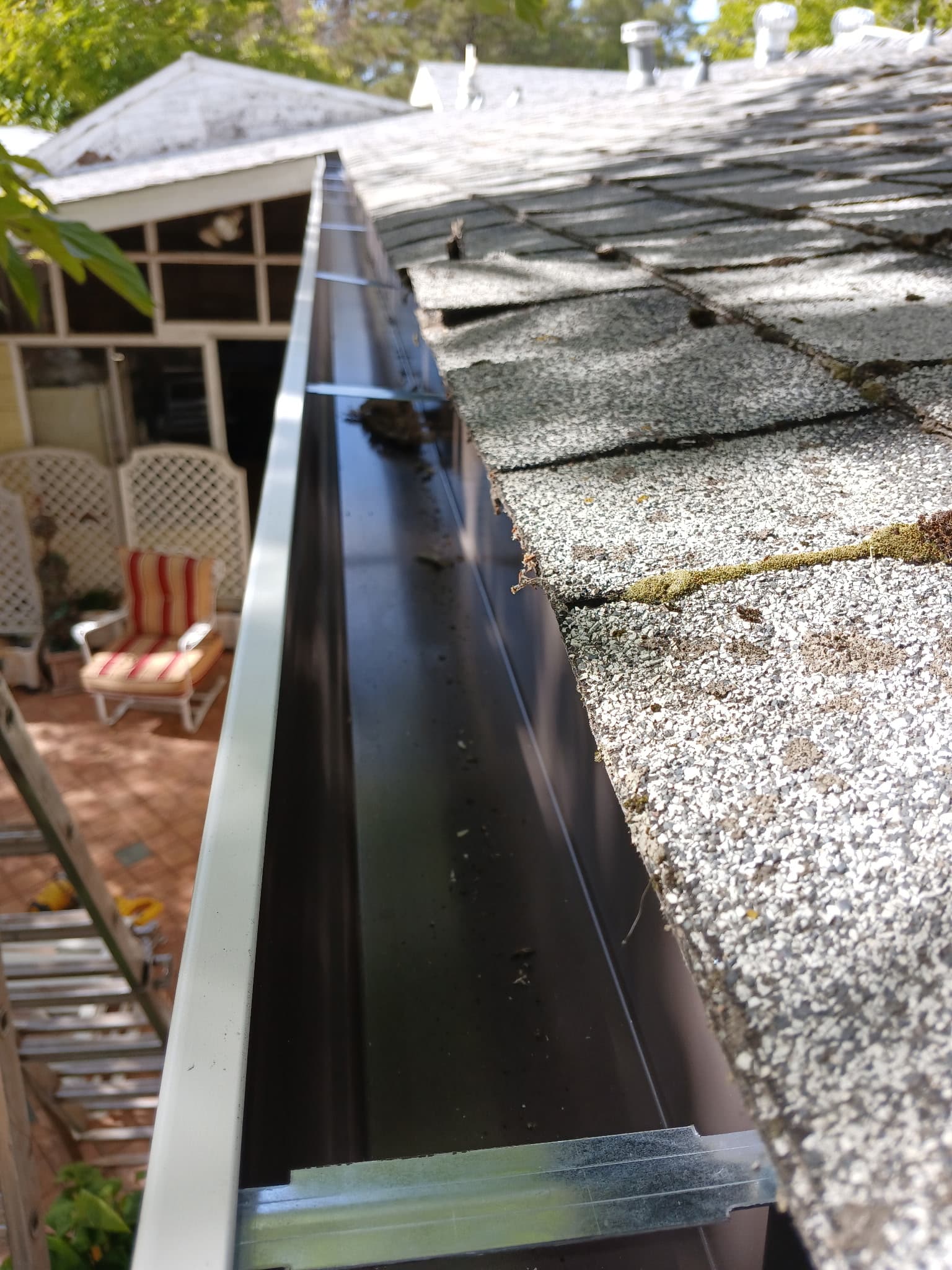 Detail of new dark brown seamless gutter installed over composition shingle roof